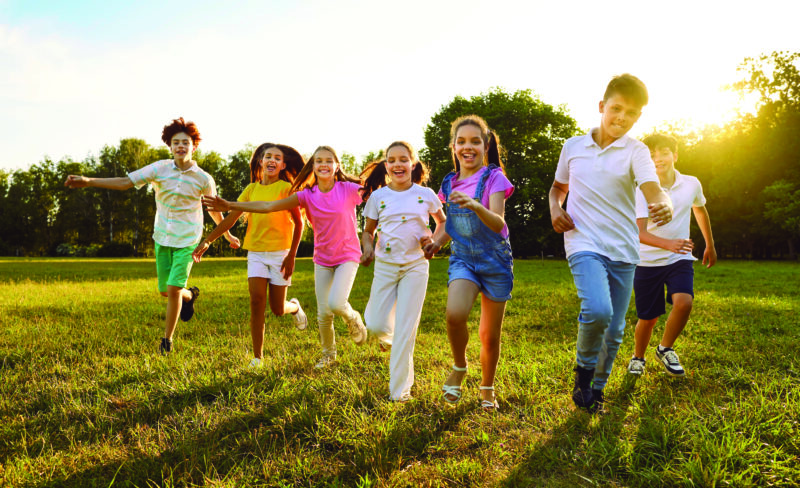 Happy, joyful, carefree kids playing together in summer. Children enjoying free time, playing and having fun. Group of cheerful little friends running on a grassy lawn in a green sunny park